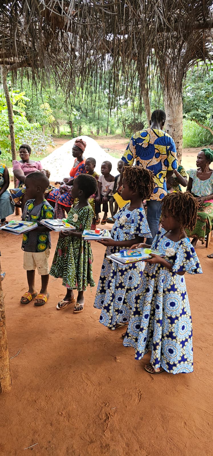 Children proudly carrying their school supply kits under a thatched shelter